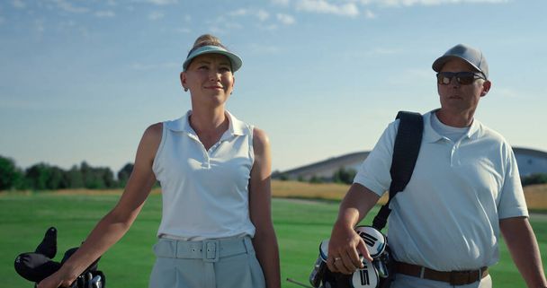 Golf players couple walk together on lush course. Rich people talking in summer sunlight close up. Two business partners club members enjoy golfing game in countryside. Wealthy lifestyle hobby concept - Foto, Imagem