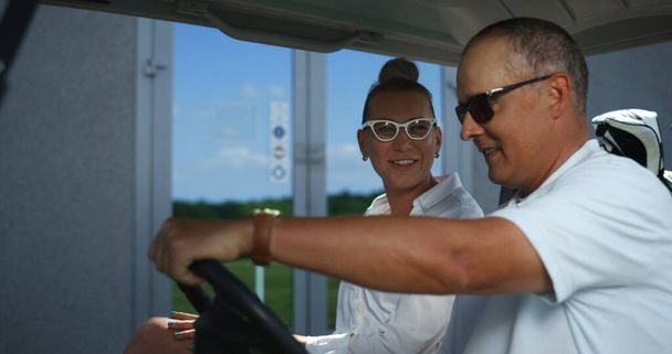 Golfisté diskutují vozík na víkendovém turnaji. Šťastný pár se chystá začít hru v golfovém autě. Usmívající se tým mluví kluby na akční kurz rekreační resort. Luxusní hobby sport koncept. - Fotografie, Obrázek