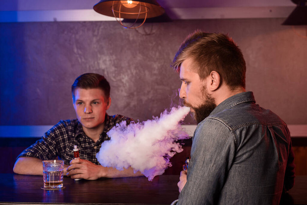 Двоє молодих чоловіків курять електронні сигарети на вейпбарі. Вейп магазин
 - Фото, зображення