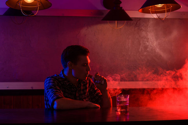 El hombre fuma un cigarrillo electrónico en la tienda de vapores. Barra de cinta. - Foto, Imagen