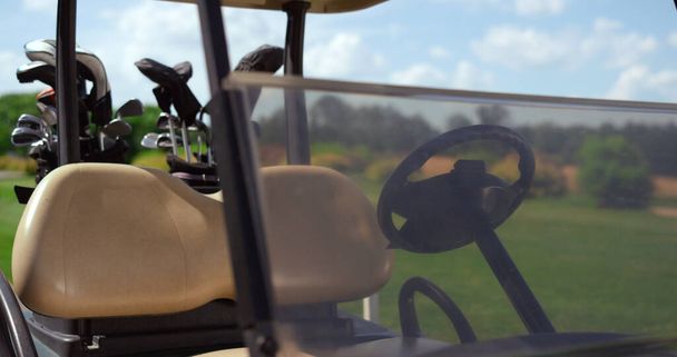 Golfkarretje uitrusting clubs op groene baan. Lege autorijdende stop bij Country Club close-up. Aandrijfstoel voorruit wiel in buggy design. Sportuitrusting accessoires op golf fairway. Luxe concept. - Foto, afbeelding