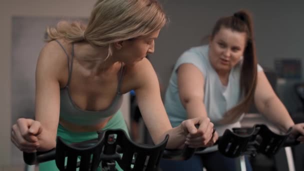 Two caucasian women ride a bikes at the gym. Shot with RED helium camera in 4K.     - Footage, Video