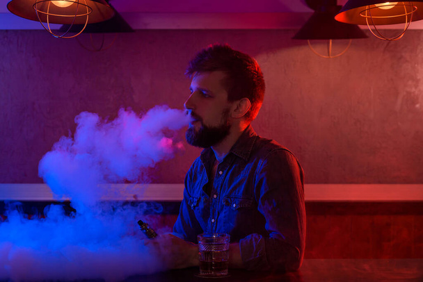 El hombre fuma un cigarrillo electrónico en la tienda de vapores. Barra de cinta. - Foto, Imagen