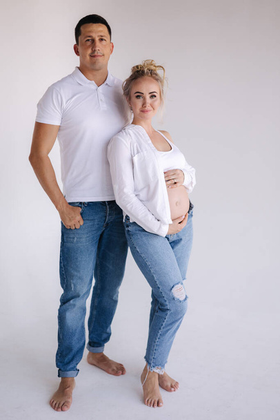 Happy future parents of man and pregnant woman puts hands on belly and waiting for beby movement in the belly. Studio photosession. Man dnd woman barefoot. Denim style. - Foto, immagini