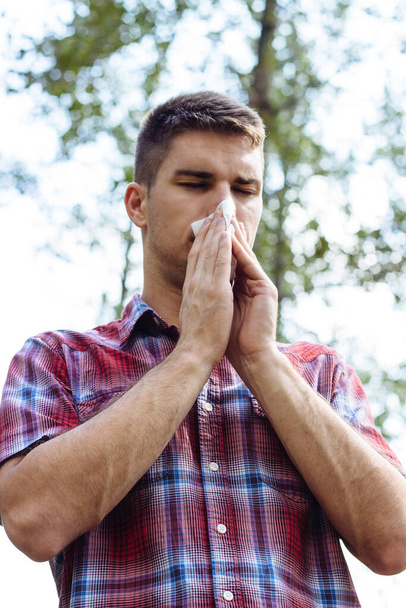 Un jeune homme allergique éternuant dans un mouchoir - Photo, image