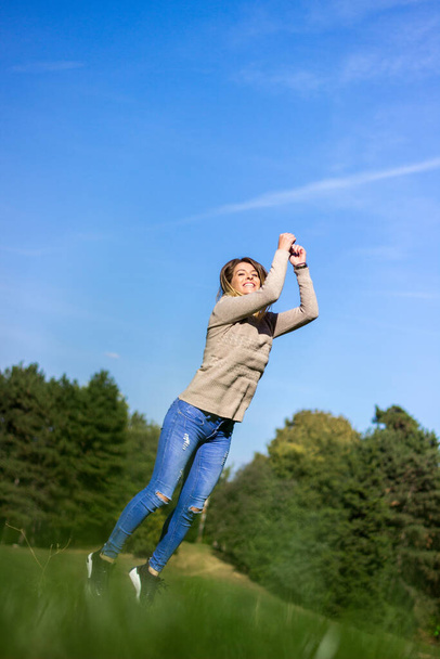 Happy young woman jumping with hands raised towards sky - Фото, зображення