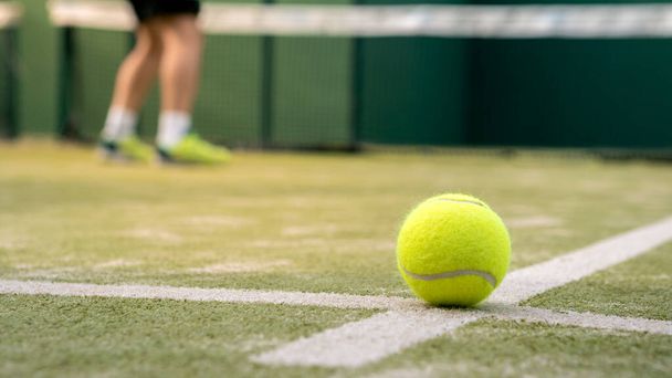 Κίτρινη μπάλα στο πάτωμα πίσω από δίχτυ κουπί σε πράσινο γήπεδο σε εξωτερικούς χώρους. Ο άνθρωπος που παίζει padel τένις. Καυκάσιος αθλητής χτυπάει μπάλες. Racquet έννοια του αθλητισμού παιχνίδι. - Φωτογραφία, εικόνα