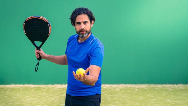Monitor de padel sosteniendo raqueta negra con pelota de tenis amarilla en la mano. Clase para estudiantes en cancha de tenis al aire libre. Hombre paddel jugador jugando un partido al aire libre - Foto, Imagen