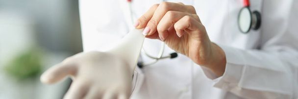 Крупним планом лікар або медсестра надягають стерильні рукавички перед роботою в клініку. Медичний працівник у формі, готовий до зустрічі. Здоров'я, концепція лікарні
 - Фото, зображення