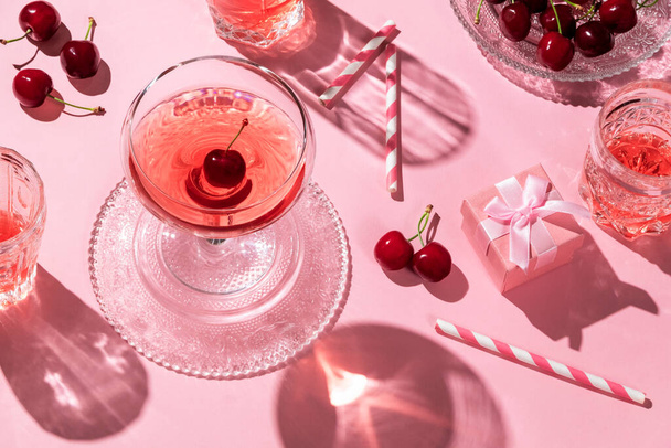 Piso festivo con bebidas de cerezas y una caja de regalo, todo en color rosa - Foto, Imagen