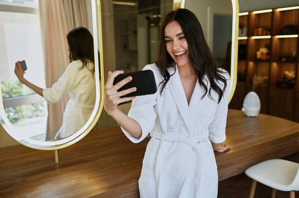 young beautiful girl in a beauty salon in a white coat makes a selfie. Bride's morning concept - Foto, immagini