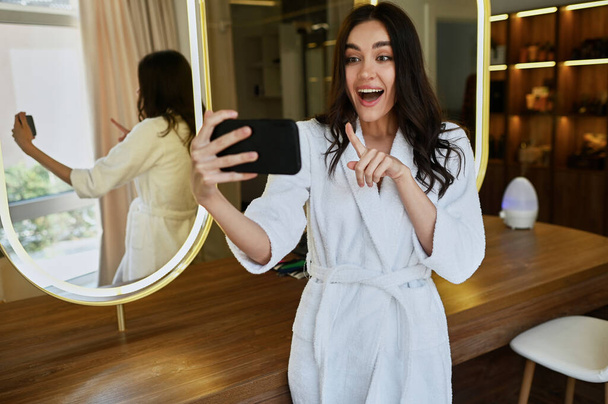 giovane bella ragazza in un salone di bellezza in un cappotto bianco fa un selfie. Concetto mattutino della sposa - Foto, immagini
