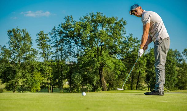 Кавказский игрок в гольф за 40 с использованием клюшки на солнечном поле для гольфа во время малого турнира.  - Фото, изображение