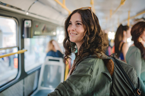 Dojeżdżająca kobieta w połowie dorosła stoi w autobusie i podróżuje komunikacją miejską. - Zdjęcie, obraz