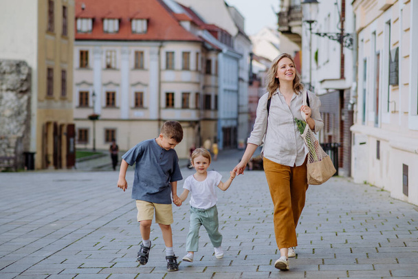 A young mother with zero waste shopping bag holding hands with her children and walking in city street street - Foto, Bild