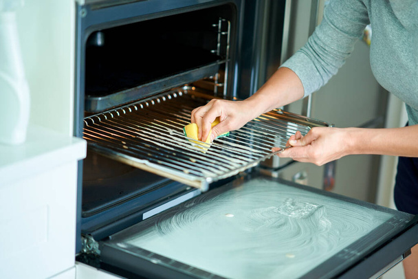 Junge Frau putzt Backofen in der Küche. Hochwertiges Foto - Foto, Bild