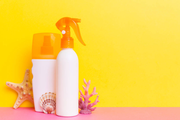Beach accessories. Moisturiser sunscreen suntan lotion bottle for UVB skincare protection in summer with seashells on colored background. Mock up with copy space. - 写真・画像