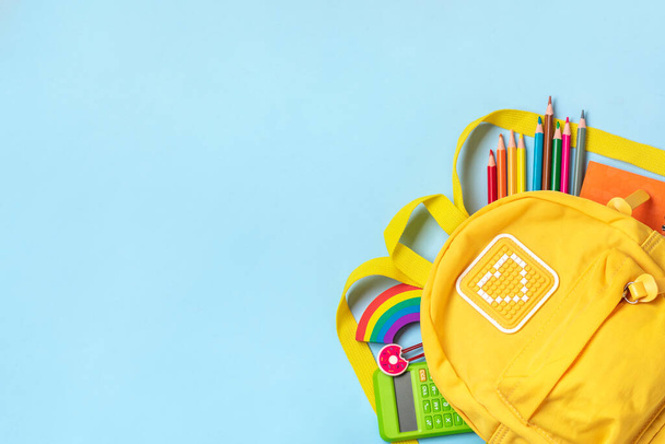 Back to school, education concept Yellow backpack with school supplies - notebook, pens, eraser rainbow, numbers isolated on blue background Top view Copy space Flat lay composition. - Photo, image