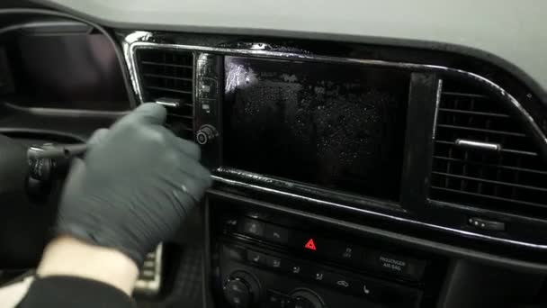 Man met zwarte handschoenen reinigt dashboard met borstel en wasmiddel zittend op de bestuurdersstoel. Schoonmaken van het dashboard. Zwarte auto paneel van auto closeup - Video