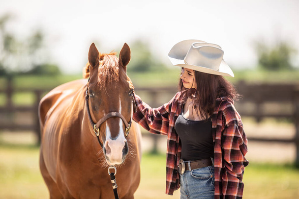 Beautiful girl strokes a horse smiling at it in a farm. - Фото, зображення