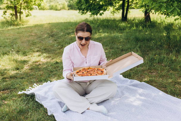 Joyeux jeune femme tenant une pizza chaude en boîte sur fond de nature. Fille attrayante se sent faim et aime le goût. Pizza entière pour moi. - Photo, image