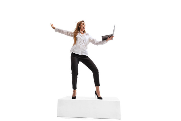 Портрет возбужденной молодой девушки, сотрудницы в официальной ткани, держащей ноутбук изолированным на белом фоне студии. Онлайн переговоры. Концепция бизнеса, успех, рост, мотивация, сотрудничество - Фото, изображение