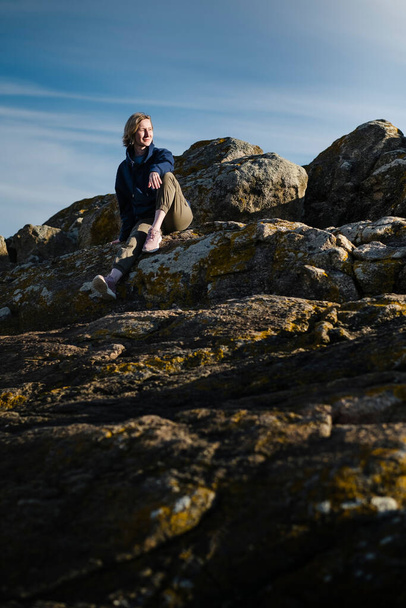A woman tourist sits on the rocks against a blue sky. - Fotó, kép