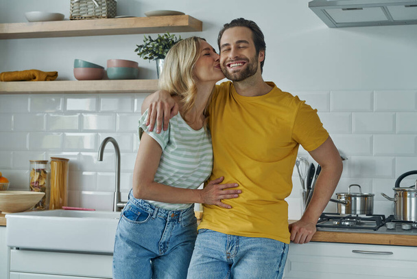 Cute couple embracing and kissing while standing at the domestic kitchen - Valokuva, kuva