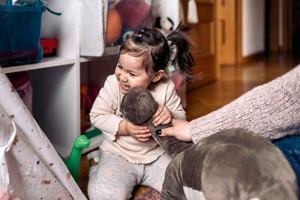 Stock photo of cute little girl having fun at home playing with her cuddle toys. - 写真・画像