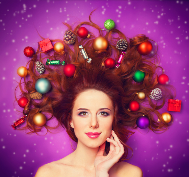 Beautiful redhead girl with christmas toys on violet background. - Photo, Image