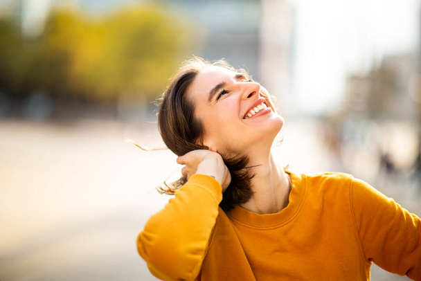 Retrato de una joven feliz riendo en la calle con la mano en el pelo y mirando hacia arriba - Foto, Imagen