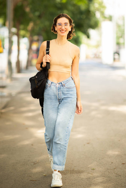 Retrato vertical de una joven de moda que camina con un bolso afuera en la calle de la ciudad - Foto, Imagen