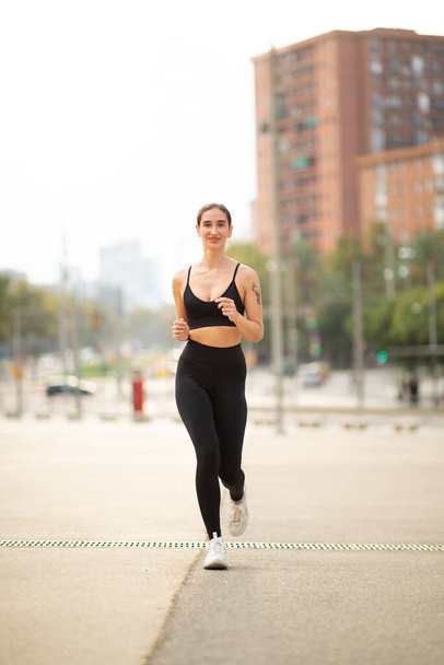 Portrait vertical complet du corps de la jeune femme en forme dans les vêtements de sport faisant de l'entraînement de course dans la ville - Photo, image