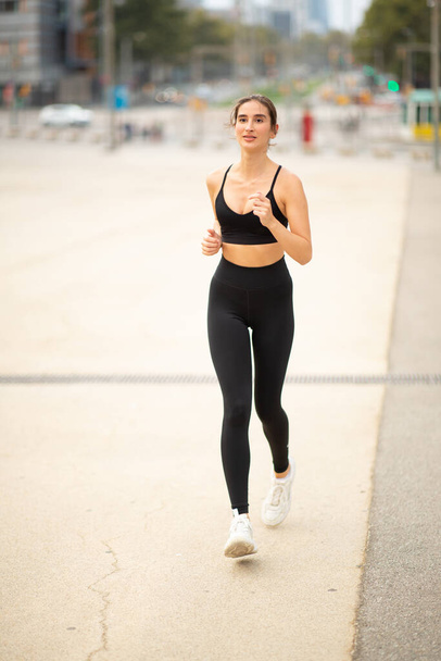 Ritratto verticale a figura intera di giovane donna attiva in abbigliamento sportivo che fa esercizio di corsa in città - Foto, immagini