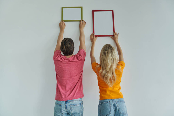 Rear view of couple hanging picture frames at the wall - Foto, Imagem