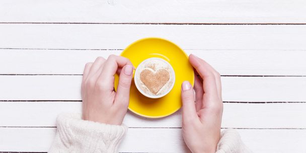 Vrouwelijke handen met kopje koffie op houten tafel. - Foto, afbeelding