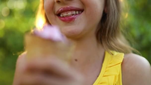 Chica feliz con frenillos comiendo helado italiano cono sonriendo mientras descansa en el parque en el día de verano, niño disfrutando de helado al aire libre, felices fiestas, verano - Metraje, vídeo