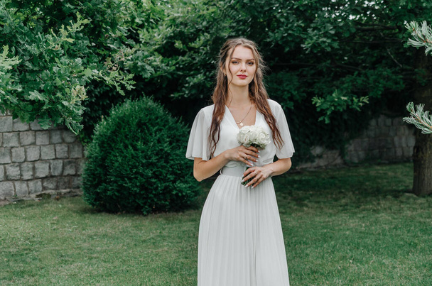 Novia en un vestido blanco con un ramo de boda blanco en la naturaleza - Foto, imagen