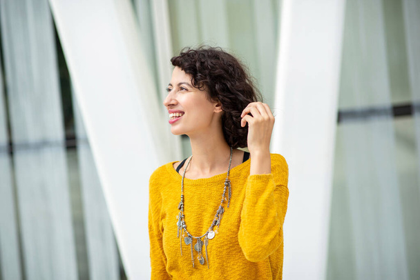 Beautiful smiling arabic woman in yellow top and souvenir necklace looking away in city - Foto, afbeelding