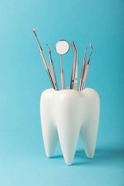 Witte gezonde tand en diverse tandheelkundige hulpmiddelen voor tandheelkundige verzorging.Tandheelkundige concept.Samenstelling op een blauwe achtergrond.Zijaanzicht. Kopieer ruimte.MOCKUP.Tandhygiëne. - Foto, afbeelding