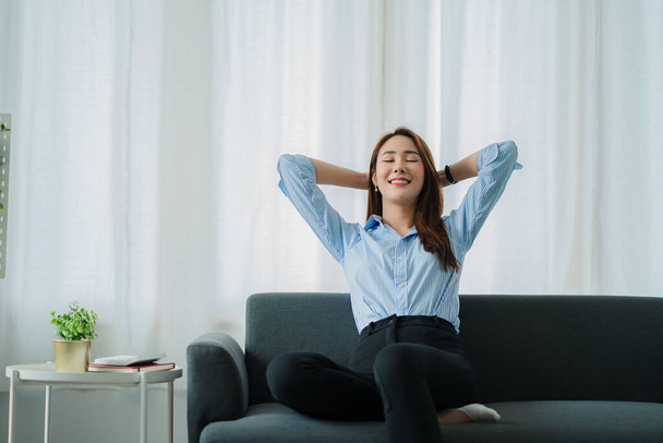 lächelnde Asiatin entspannt zu Hause auf Sofa sitzend Entspannte Lifestylefrau genießt Luxus-Sofa im Wohnzimmer. - Foto, Bild