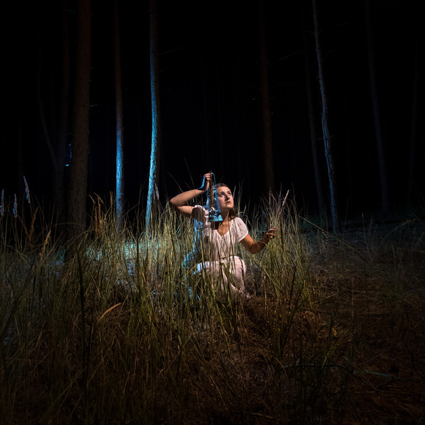 жінка в нічній сорочці сидить у високому лісі вночі з ліхтарем
 - Фото, зображення