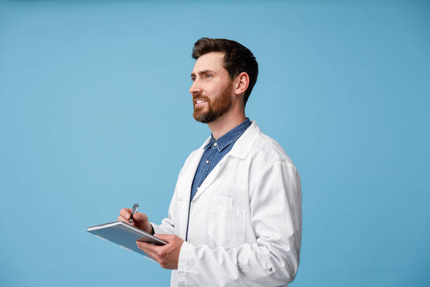 Muž Doktor si dělá lékařské poznámky do schránky ve studiu. Zdravotnictví, Medicine Worker Concept - Fotografie, Obrázek