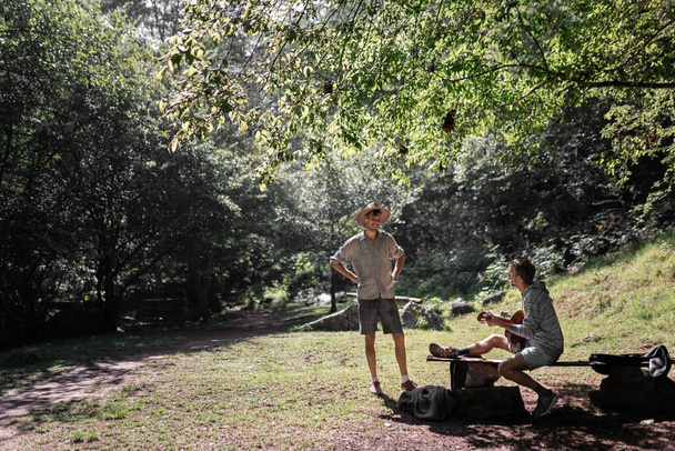 Kaksi nuorta miesystävää soittaa kitaraa luonnossa puiden ympäröimänä aurinkoisena päivänä. Ajatus hauskanpidosta luonnossa - Valokuva, kuva