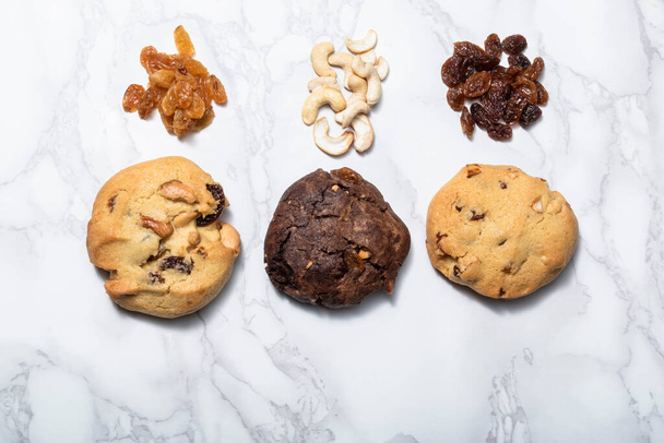 Cashew nuts raisin chocolate cookies on white marble background, close up, food and drink concept. - Фото, зображення