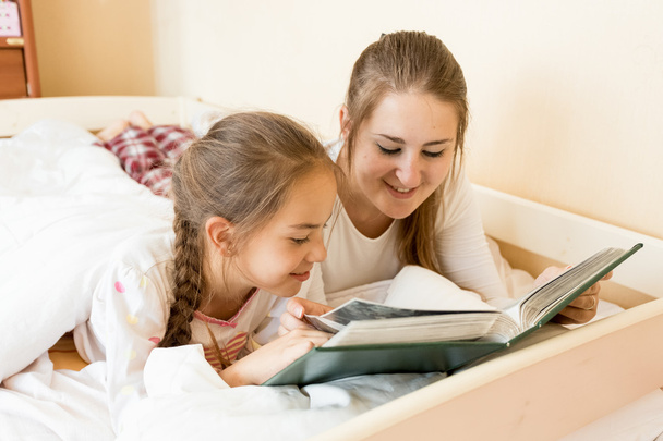 Äiti lukee iso vanha kirja tyttärelle sängyssä
 - Valokuva, kuva