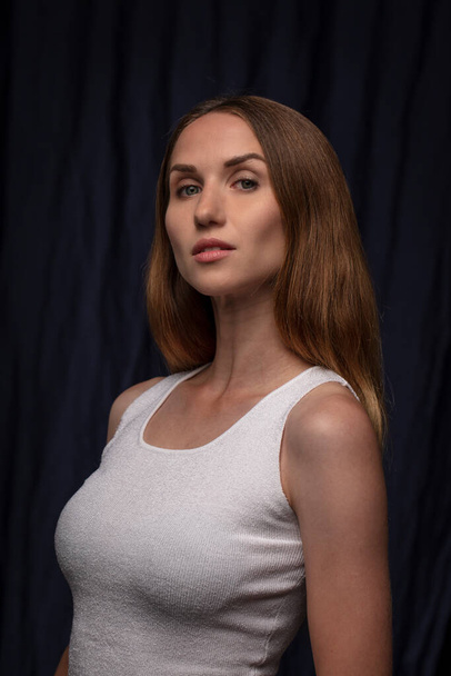 Portrait of determined young woman wearing white top looking at camera posing on dark background  - Fotografie, Obrázek