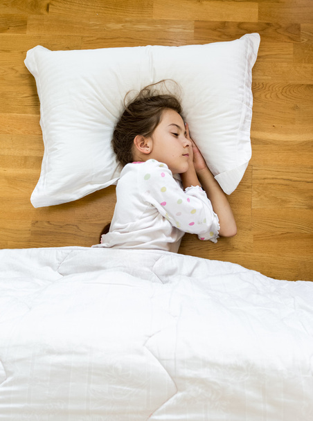 Brünettes kleines Mädchen schläft auf dem Boden mit Decke bedeckt - Foto, Bild