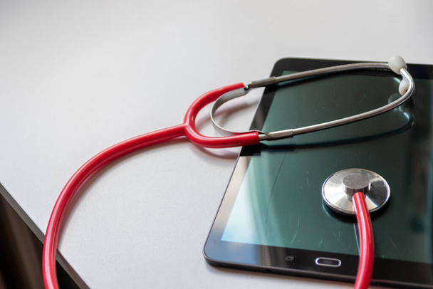 黒のタブレットデバイス上の赤い聴診器は、最新の機器や技術とデジタル医師やデジタル回復診断のためのクラウドデータセキュリティ上の健康記録やデジタル患者記録を示しています - 写真・画像