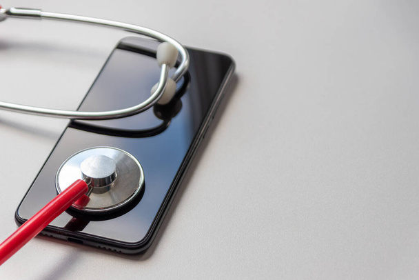 Czerwony stetoskop na czarnym smartfonie reprezentuje dokumentację zdrowotną i cyfrową dokumentację pacjenta z urządzeniami mobilnymi dla lekarzy cyfrowych oraz cyfrową diagnostykę z nowoczesnym sprzętem i technologią - Zdjęcie, obraz